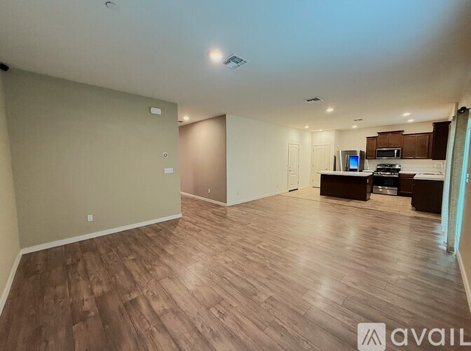 A spacious living room with wooden flooring and a kitchen area in the background.