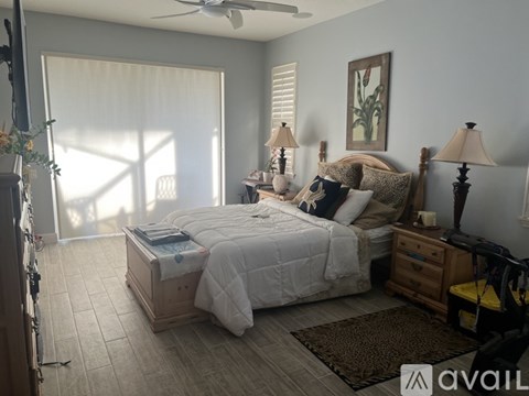 A bedroom with a large bed, a ceiling fan, and a window with blinds.