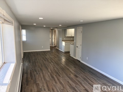A spacious room with wood flooring and a kitchen area in the background.
