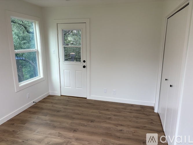 A room with a white door and a window with a view of trees.