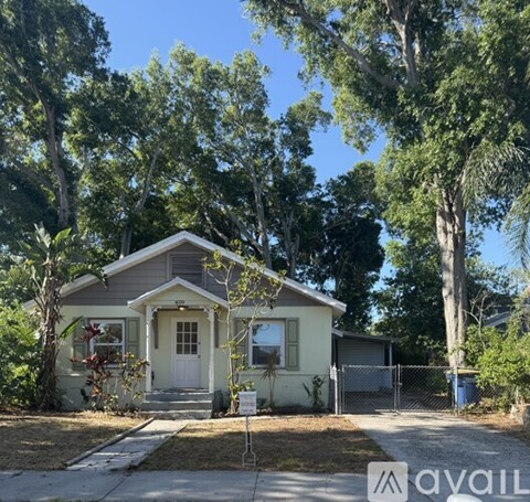 A house with a white door is surrounded by trees and has a fence.