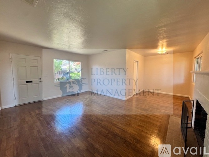 A room with wooden floors and a white ceiling with a door on the left and a window on the right.