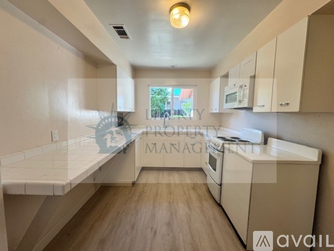 A kitchen with white countertops and wooden flooring.