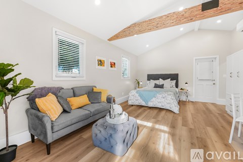 A living room with a grey couch and a bed in the background.