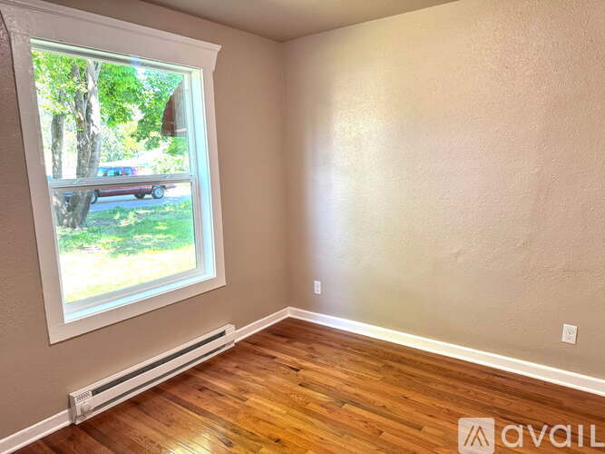 A room with a window showing a view of a car and trees outside.