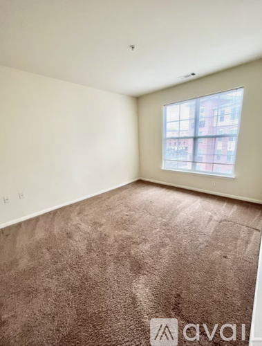 A room with a brown carpet and a window showing a building outside.