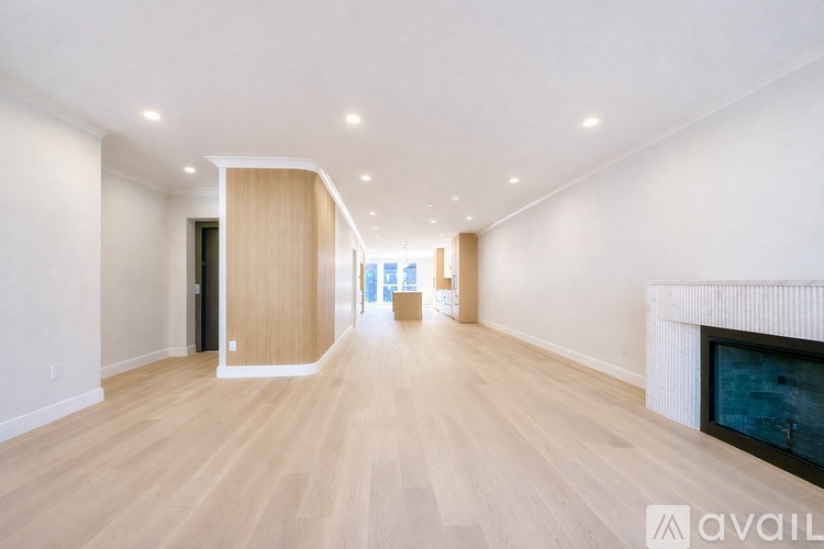 A spacious room with wooden floors and a fireplace on the right side.