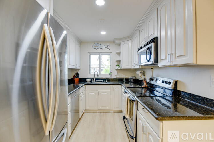 A kitchen with a stainless steel refrigerator and black countertops.