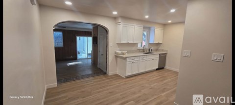 A kitchen with white cabinets and a wooden floor is available for rent.
