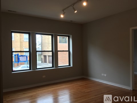 A room with wooden floors and three windows overlooking a street.