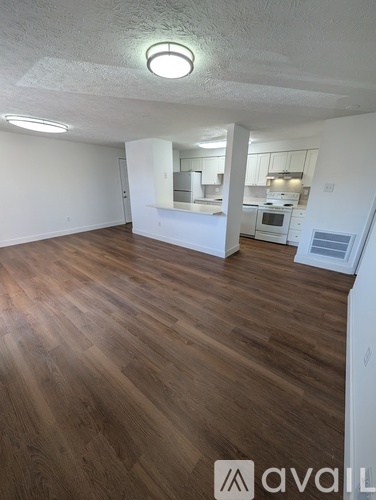 A room with wooden flooring and a kitchen area in the background.