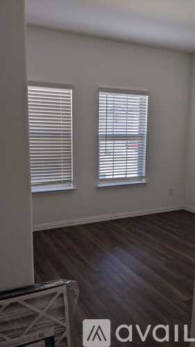 A room with wooden floors and two windows with blinds.