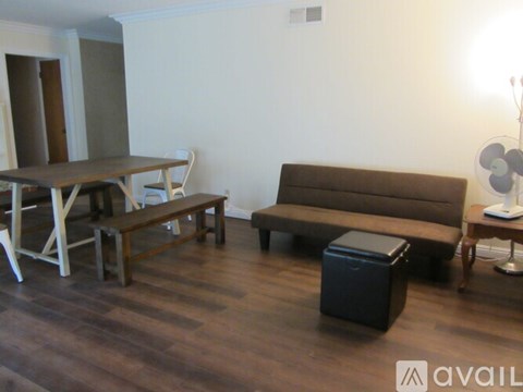 A living room with a brown couch, a wooden table, and a black trash bin.