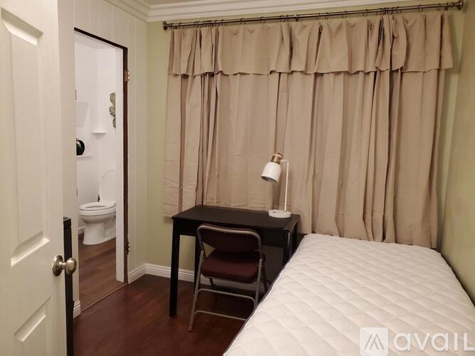 A small bedroom with a bed, desk, chair, and toilet.