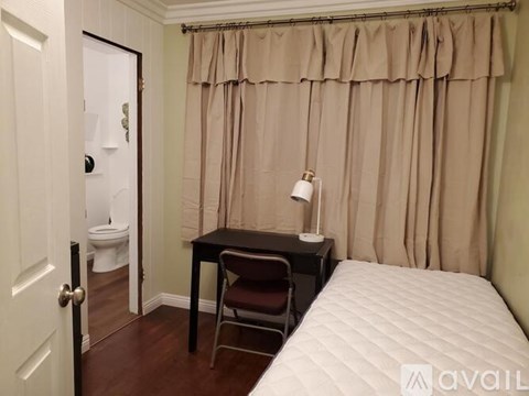 A small bedroom with a bed, desk, chair, and toilet.