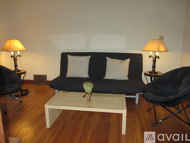 A living room with a black couch, a white coffee table, and two black chairs.