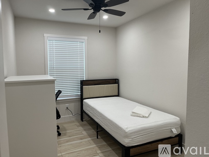 A bedroom with a bed, a ceiling fan, and a window with blinds.