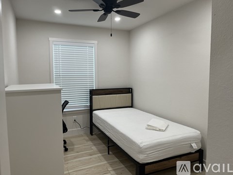 A bedroom with a bed, a ceiling fan, and a window with blinds.