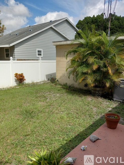 A house with a grey roof and a white fence with a small tree in front of it.