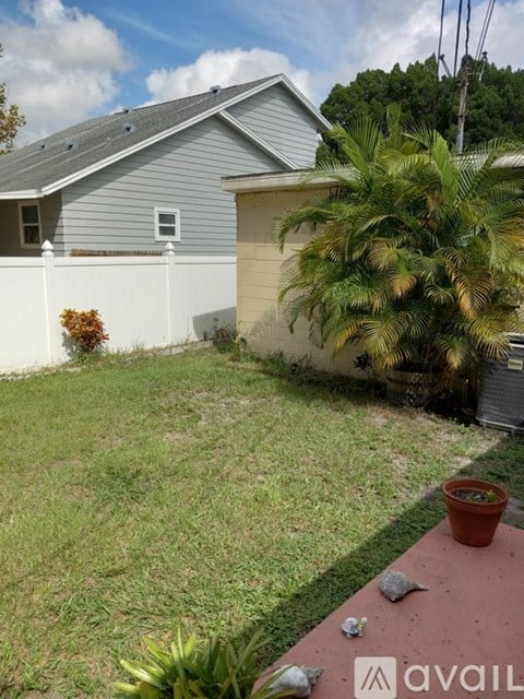 A house with a grey roof and a white fence with a small tree in front of it.