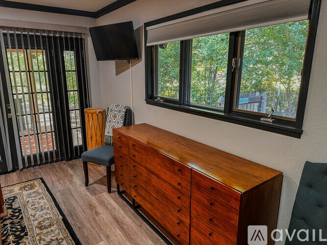 A room with a wooden dresser and a window with a view of trees.