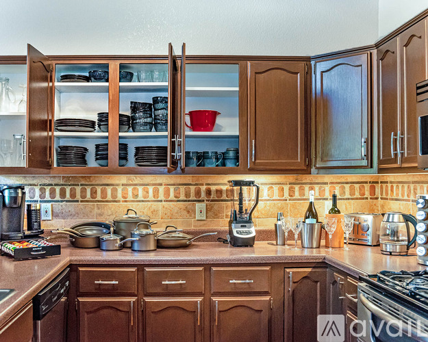A kitchen with brown cabinets and counters has a variety of cookware on the counter.