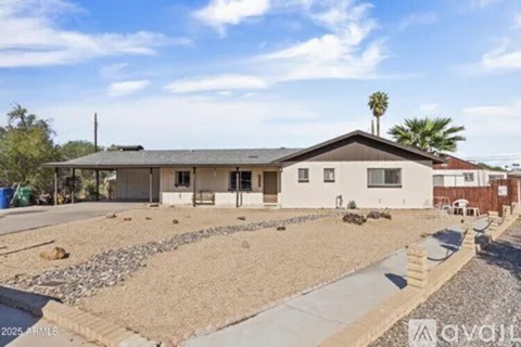 A house with a gravel driveway and a palm tree in the background.