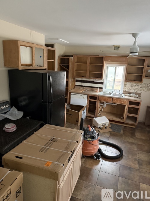 A kitchen under renovation with a black fridge, a vacuum cleaner and cardboard boxes.
