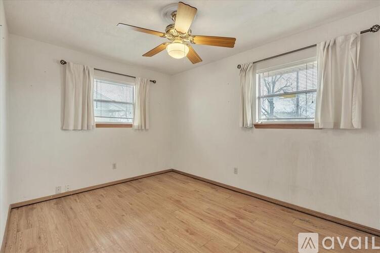 A room with a ceiling fan and two windows.