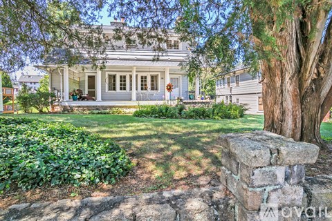 A white house with a porch and a tree in front.