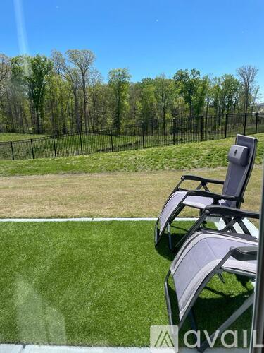 Two chairs are on a lawn with a fence and trees in the background.