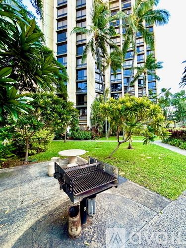 A bench with wheels is in front of a building with a green lawn.