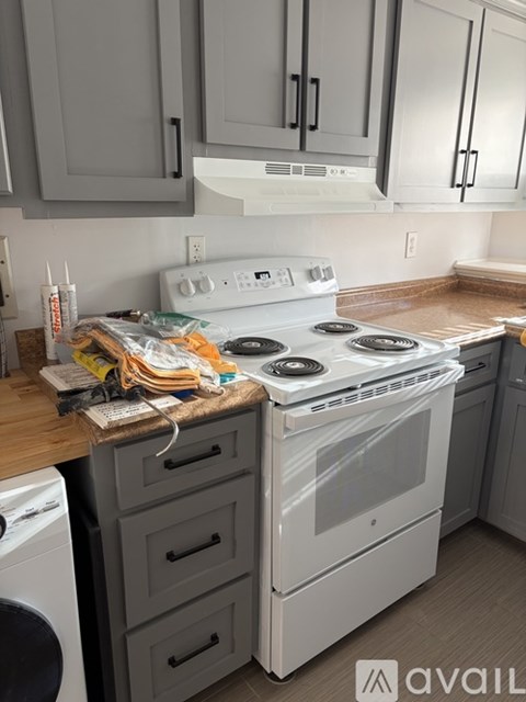A white stove top oven with a glass door is in a kitchen with a washing machine under a counter.
