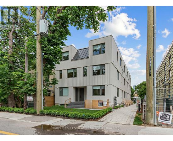 A modern building with a flat roof and large windows is surrounded by greenery and trees.