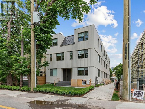 A modern building with a flat roof and large windows is surrounded by greenery and trees.