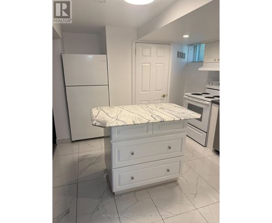 A white kitchen with a fridge, stove, and a bed.