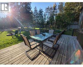 A wooden deck with a glass table and chairs is surrounded by trees.