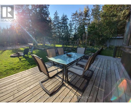 A wooden deck with a glass table and chairs is surrounded by trees.