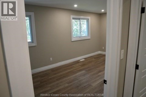 A room with wooden flooring and two windows.