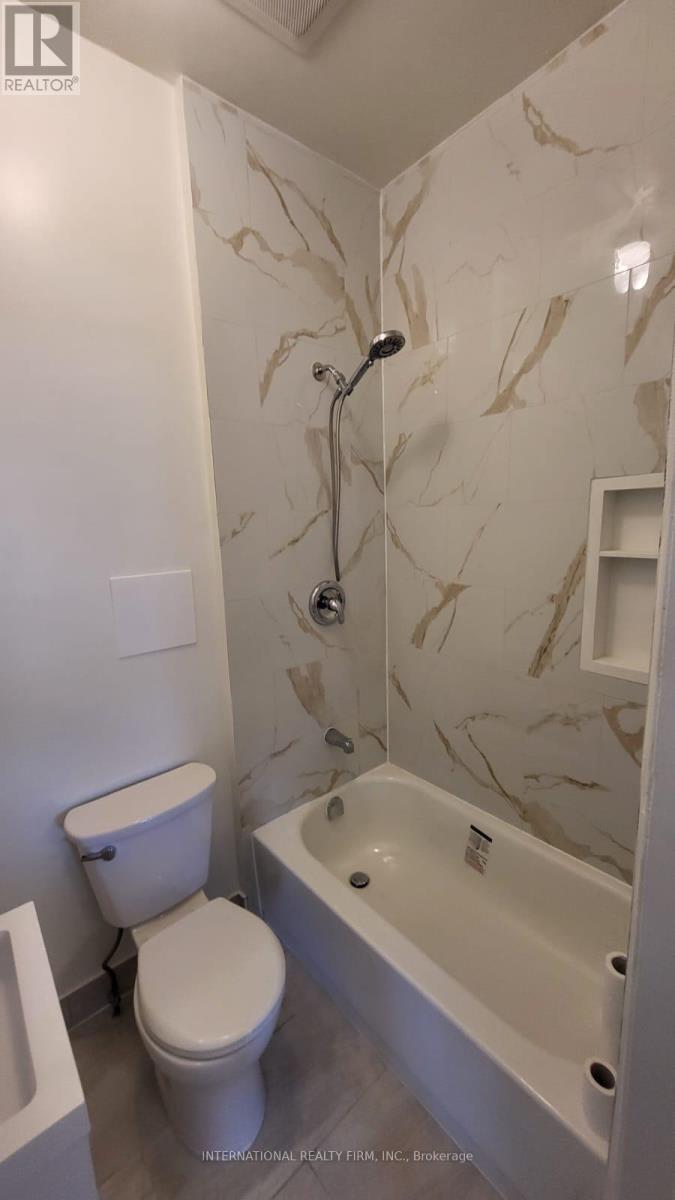 A white toilet sits next to a bathtub in a bathroom with marble wallpaper.