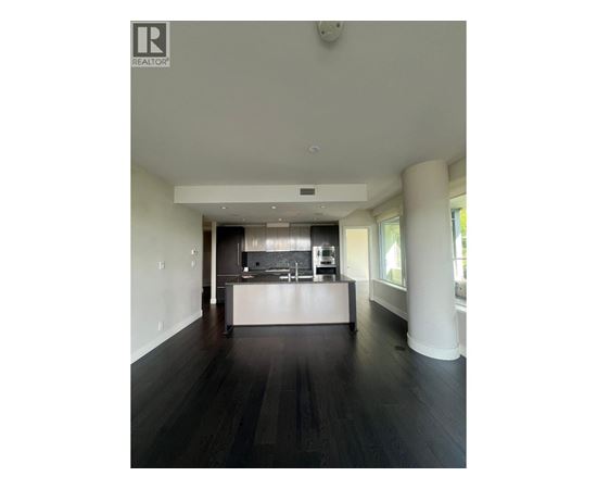 A spacious kitchen with dark wood floors and white walls.