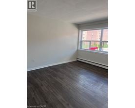 A room with wooden flooring and a window overlooking a red car and a building.