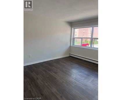 A room with wooden flooring and a window overlooking a red car and a building.