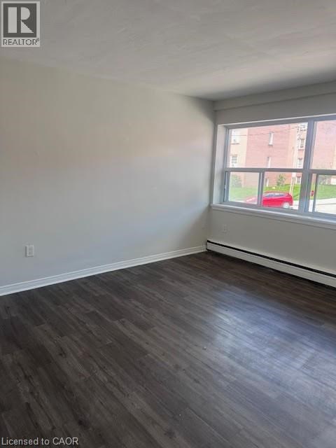 A room with wooden flooring and a window overlooking a red car and a building.