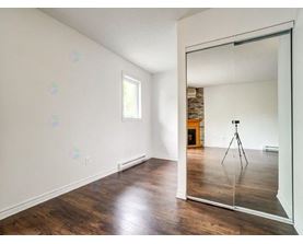 A room with wooden floors and a large mirror reflecting a tripod.