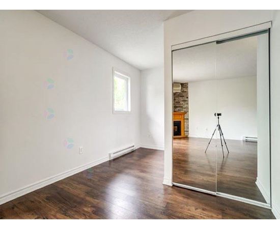 A room with wooden floors and a large mirror reflecting a tripod.