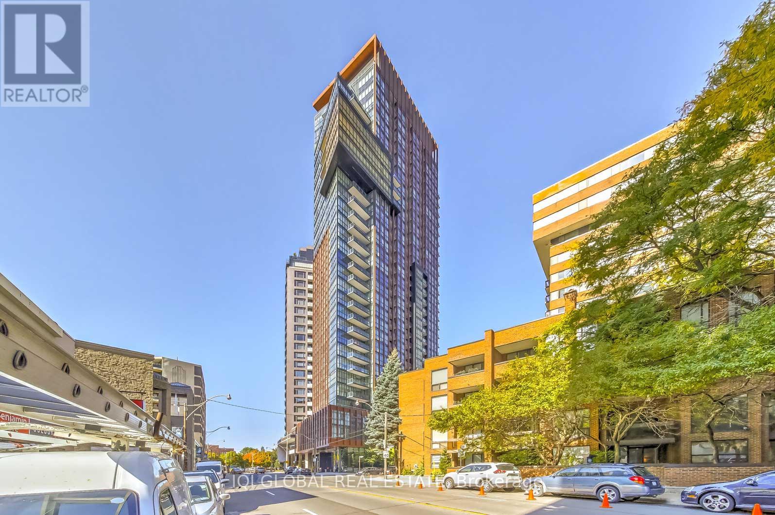 A tall building with a glass facade stands in the middle of a street lined with parked cars.