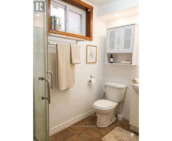 A white toilet sits in a small bathroom with a white cabinet and a window.