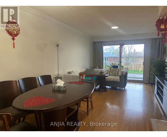 A dining room with a table and chairs and a sofa in the background.