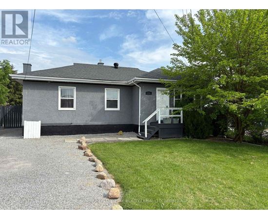 A grey house with a gravel driveway in front.